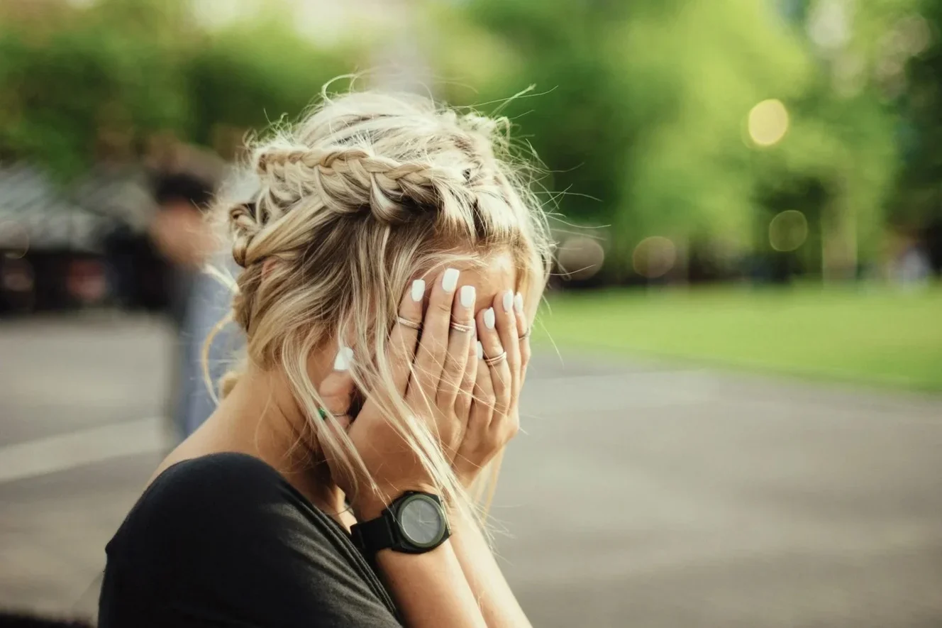 A woman covering her face with both hands outdoors.