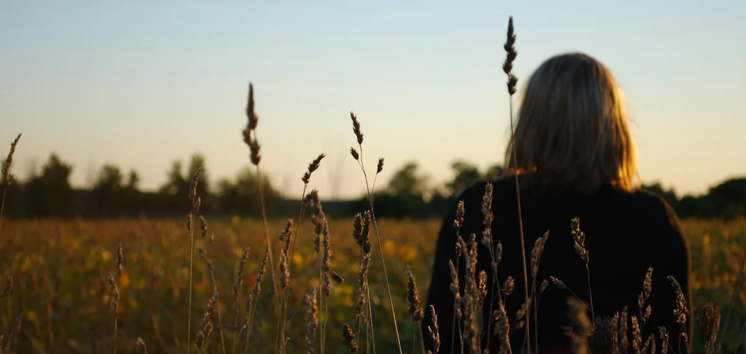 A woman sitting alone in a field looking at a sunset sky