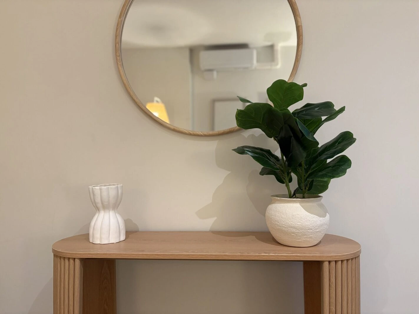 A table with a plant, a vase and a round mirror.