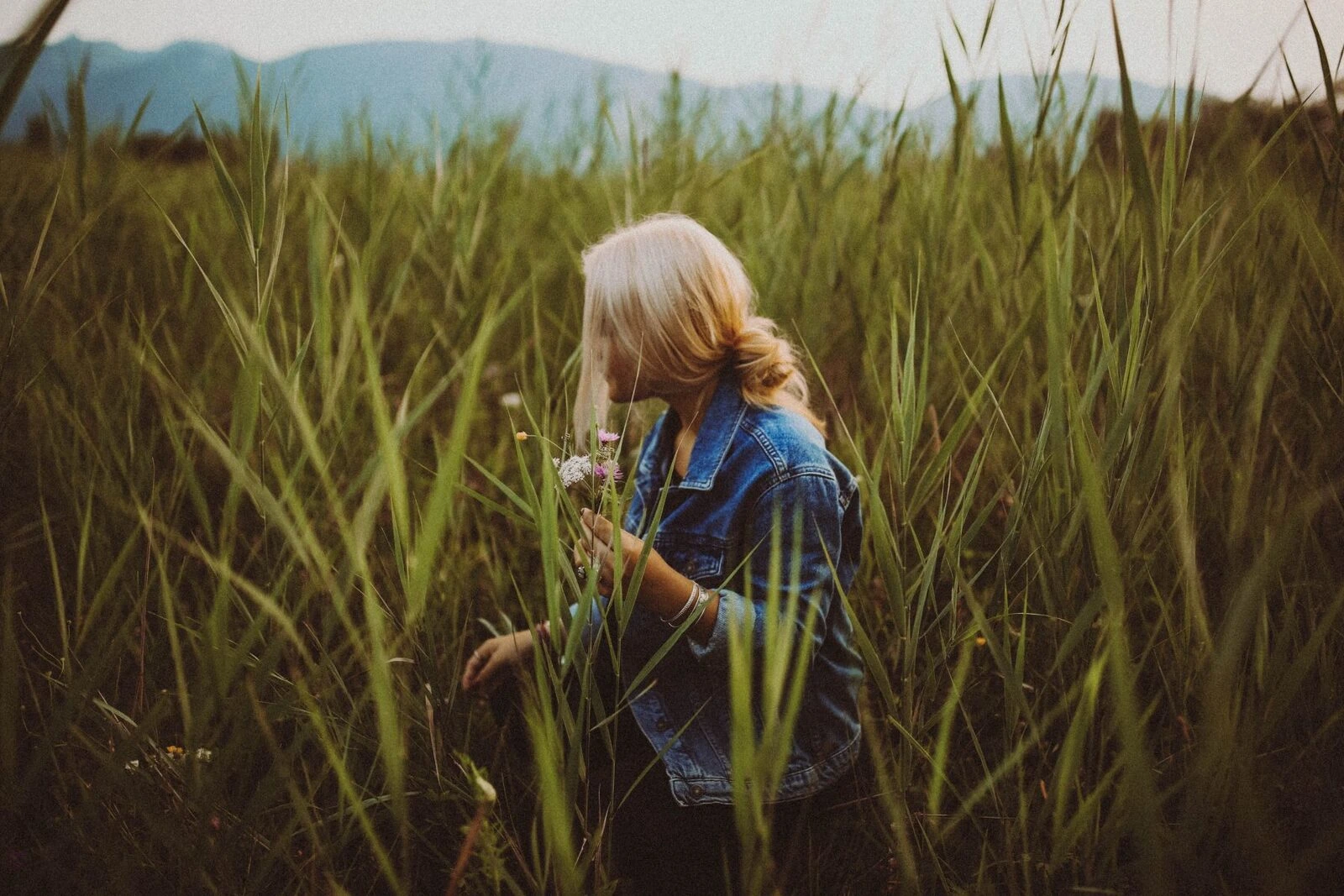 A woman holding flowers while standing in tall grass.