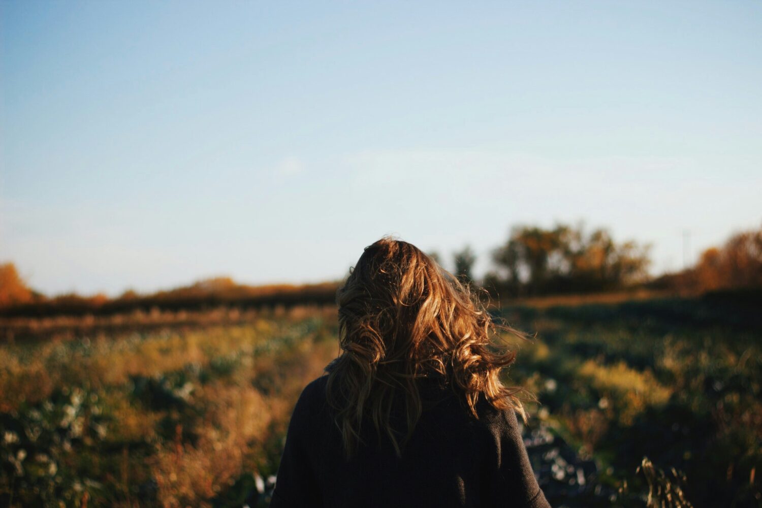 Back of a young women walking in a field in the afternoon