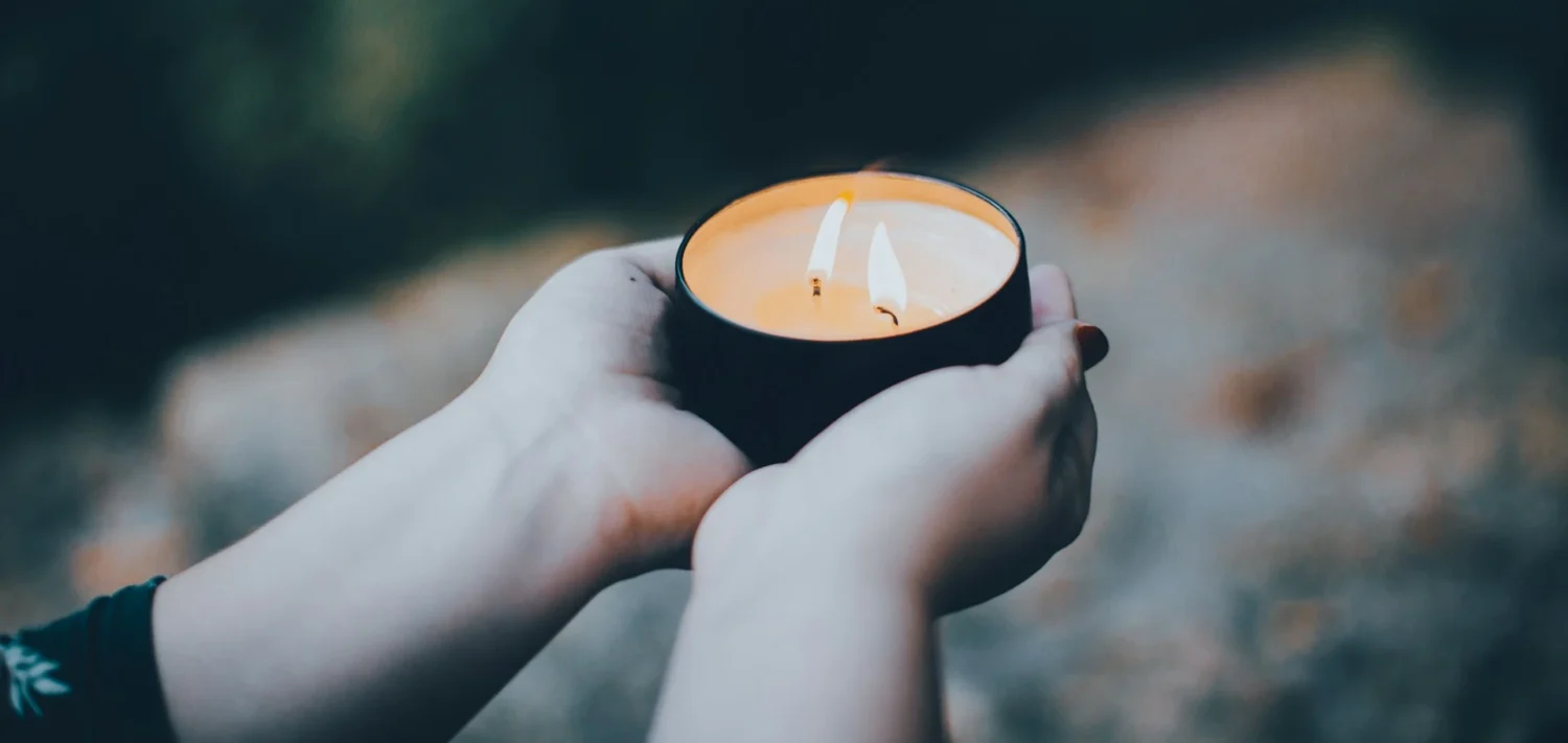 Two hands holding a lit candle