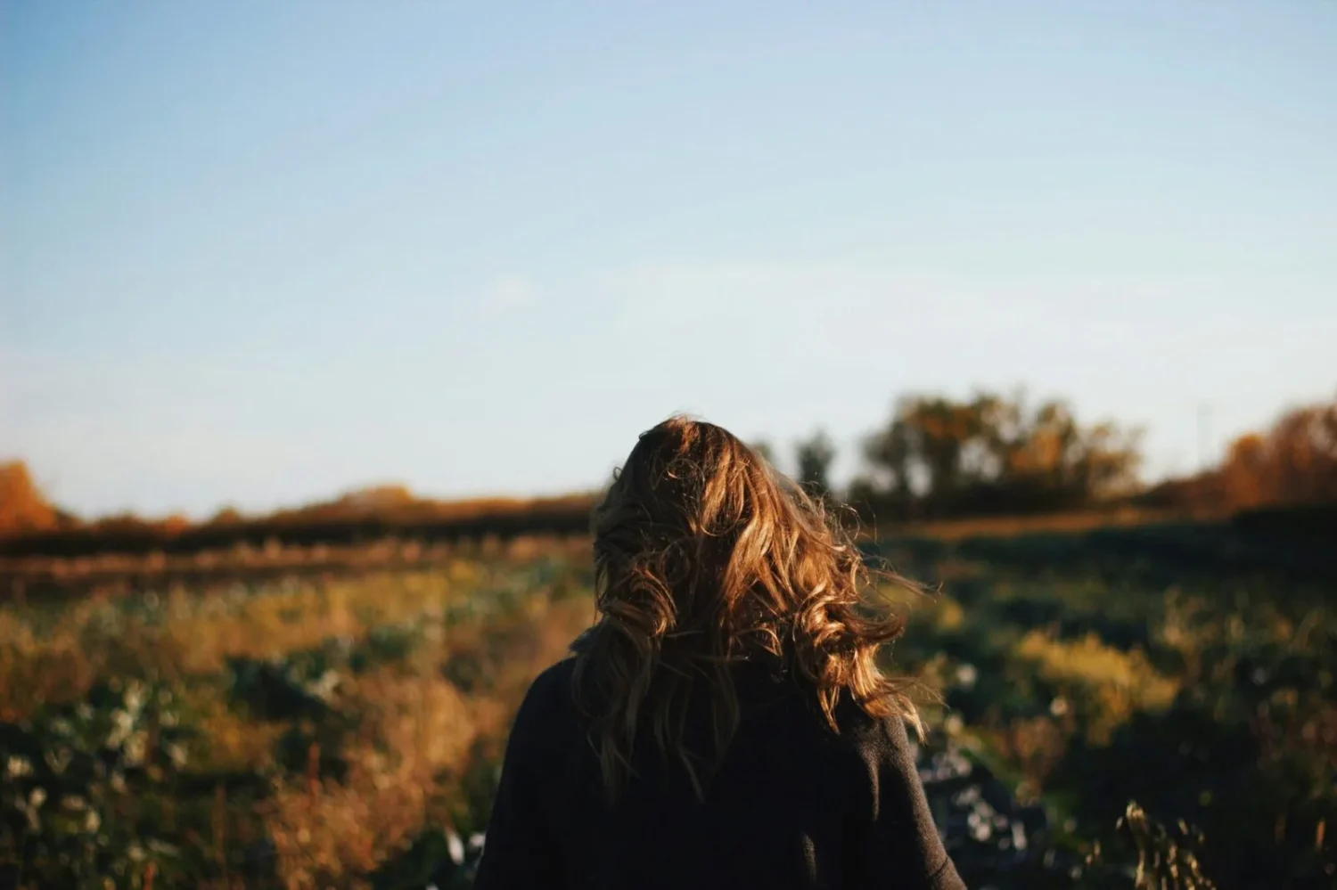A woman standing in a grassy field facing away.