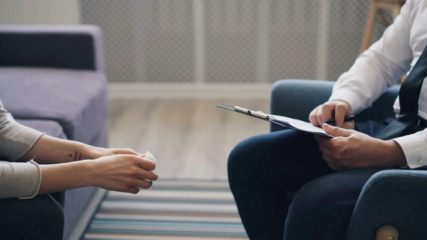 A person sitting across from a man holding a clipboard 