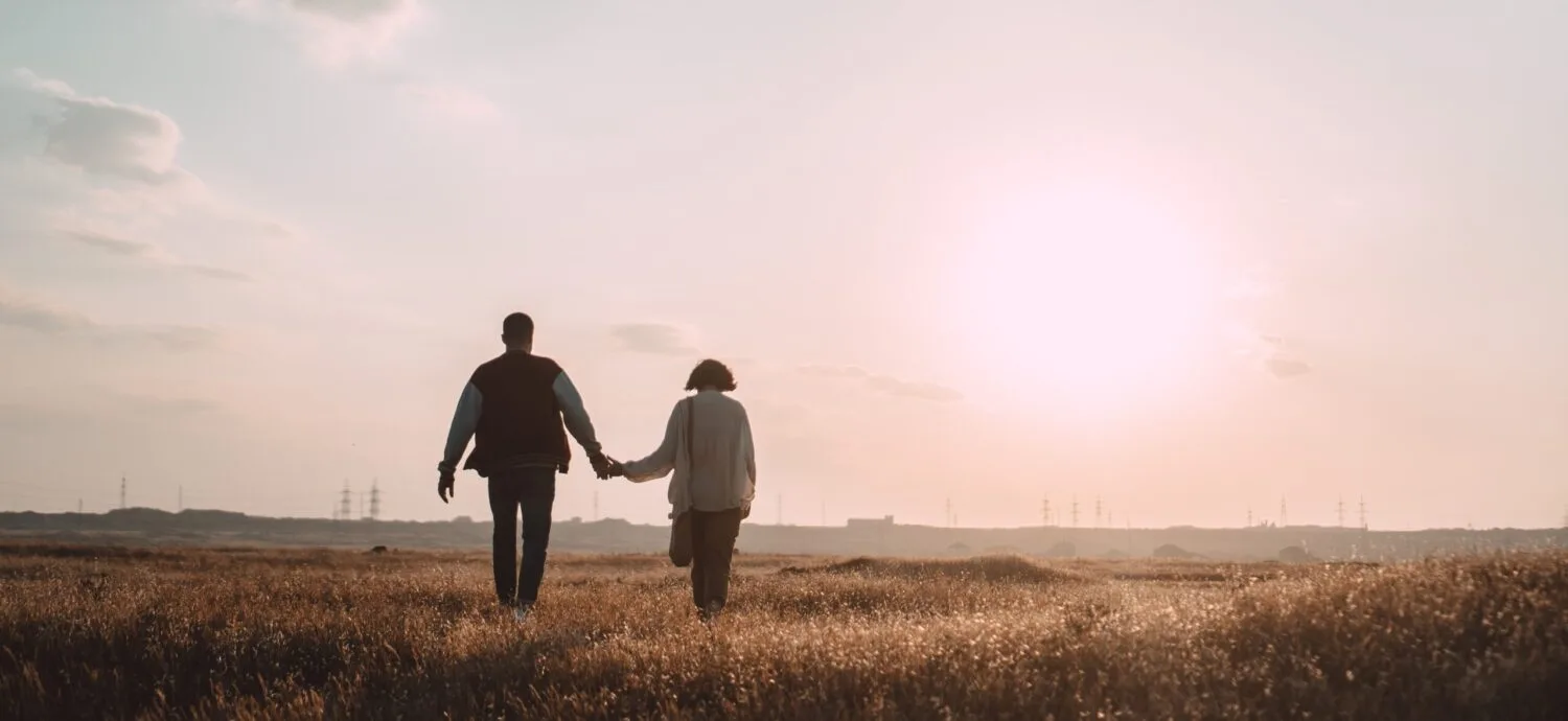Two people holding hands while walking through a field.
