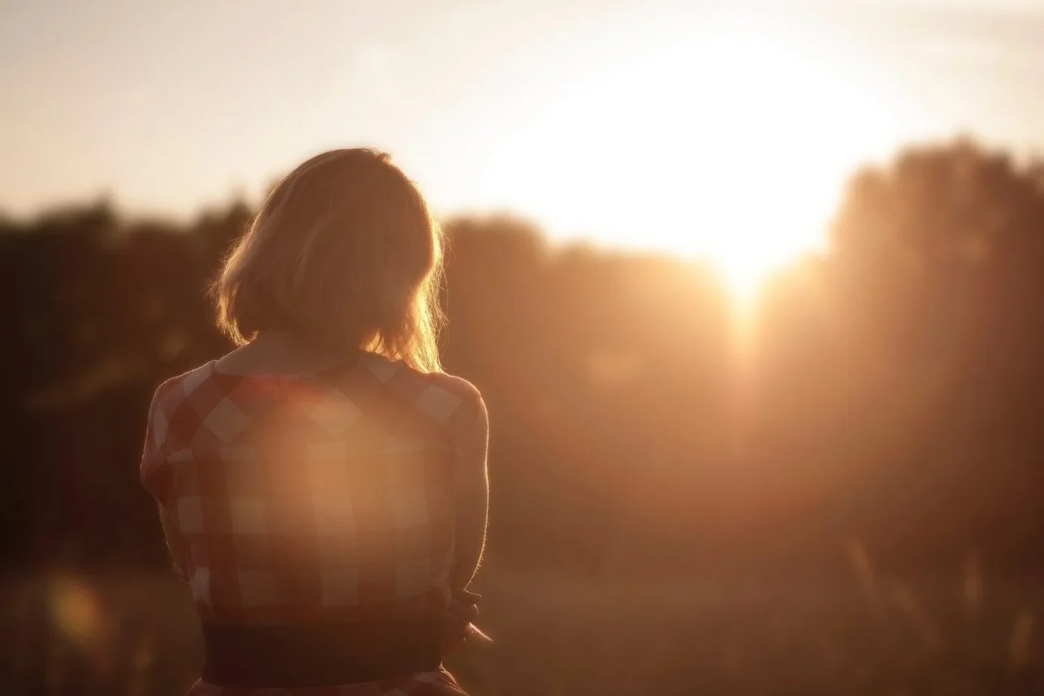 Woman facing the sunset while standing in a field.