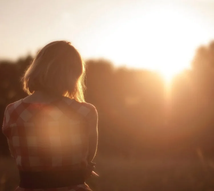 Woman facing the sunset while standing in a field.