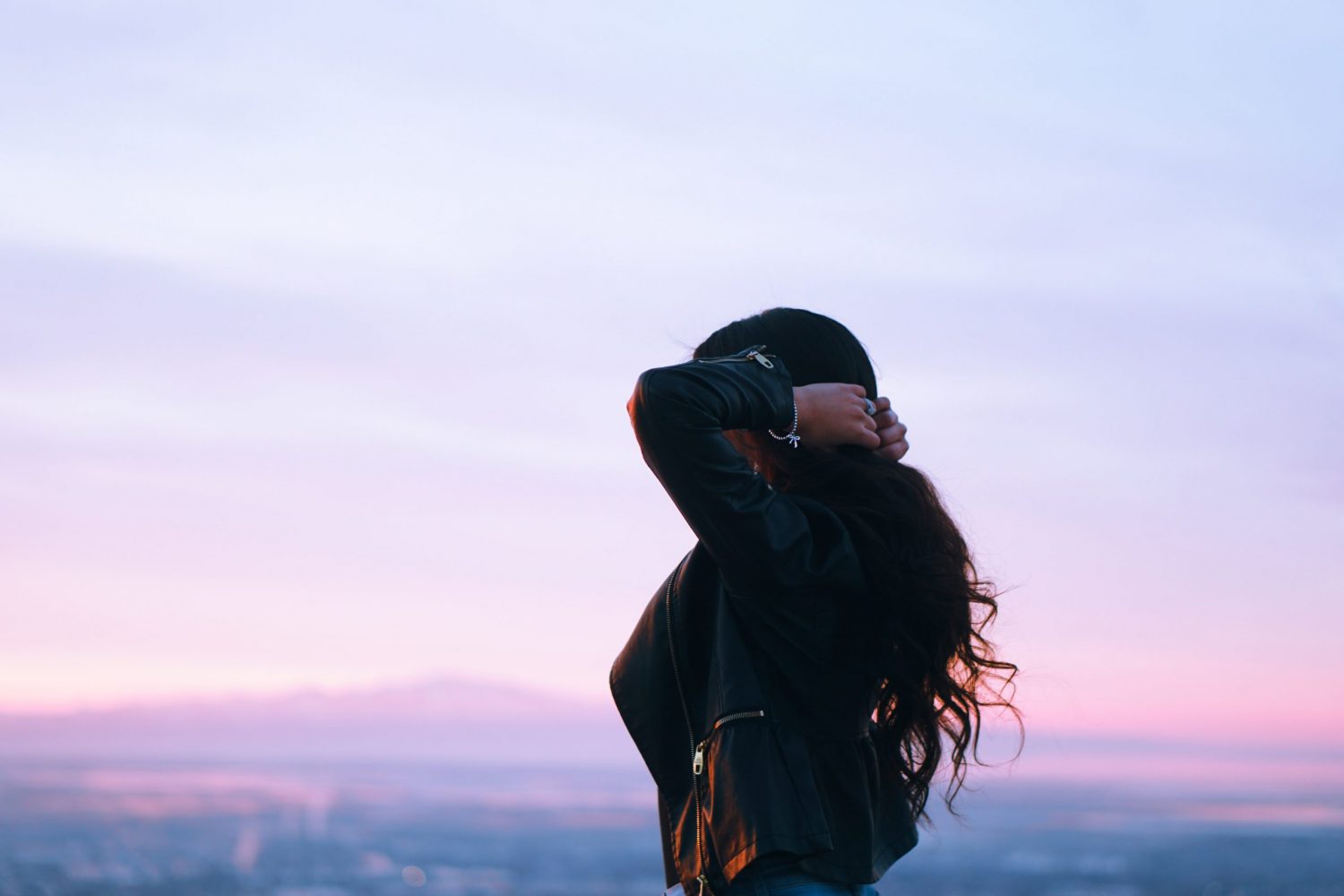 women holding her hair looking at sunset