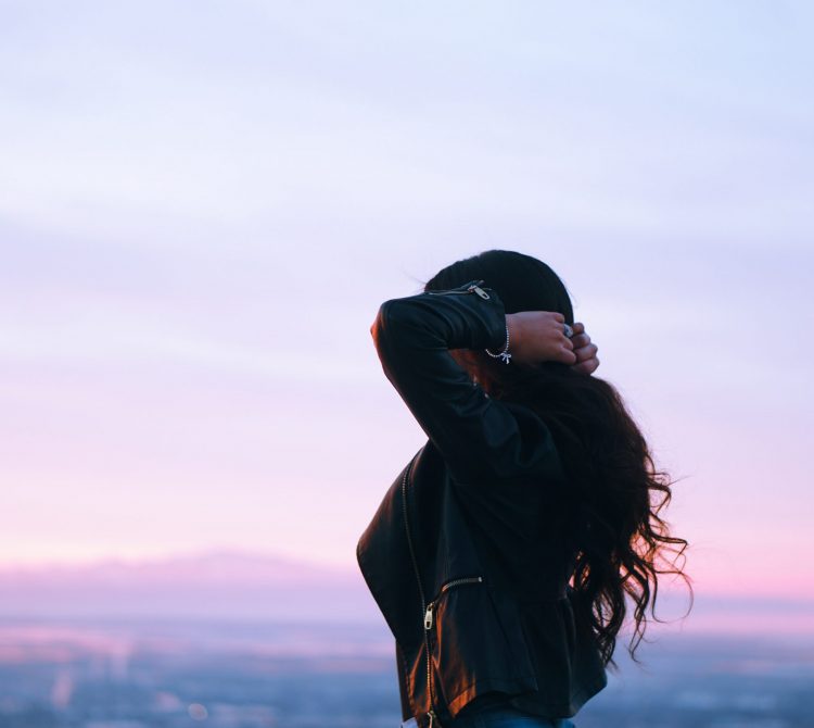 women holding her hair looking at sunset