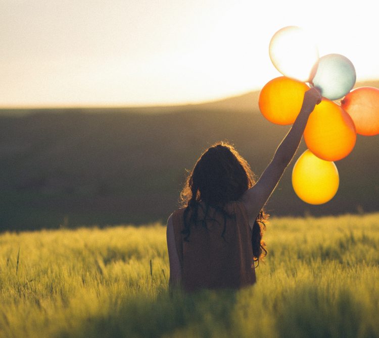 Girl holding balloons in field creating a happiness spike