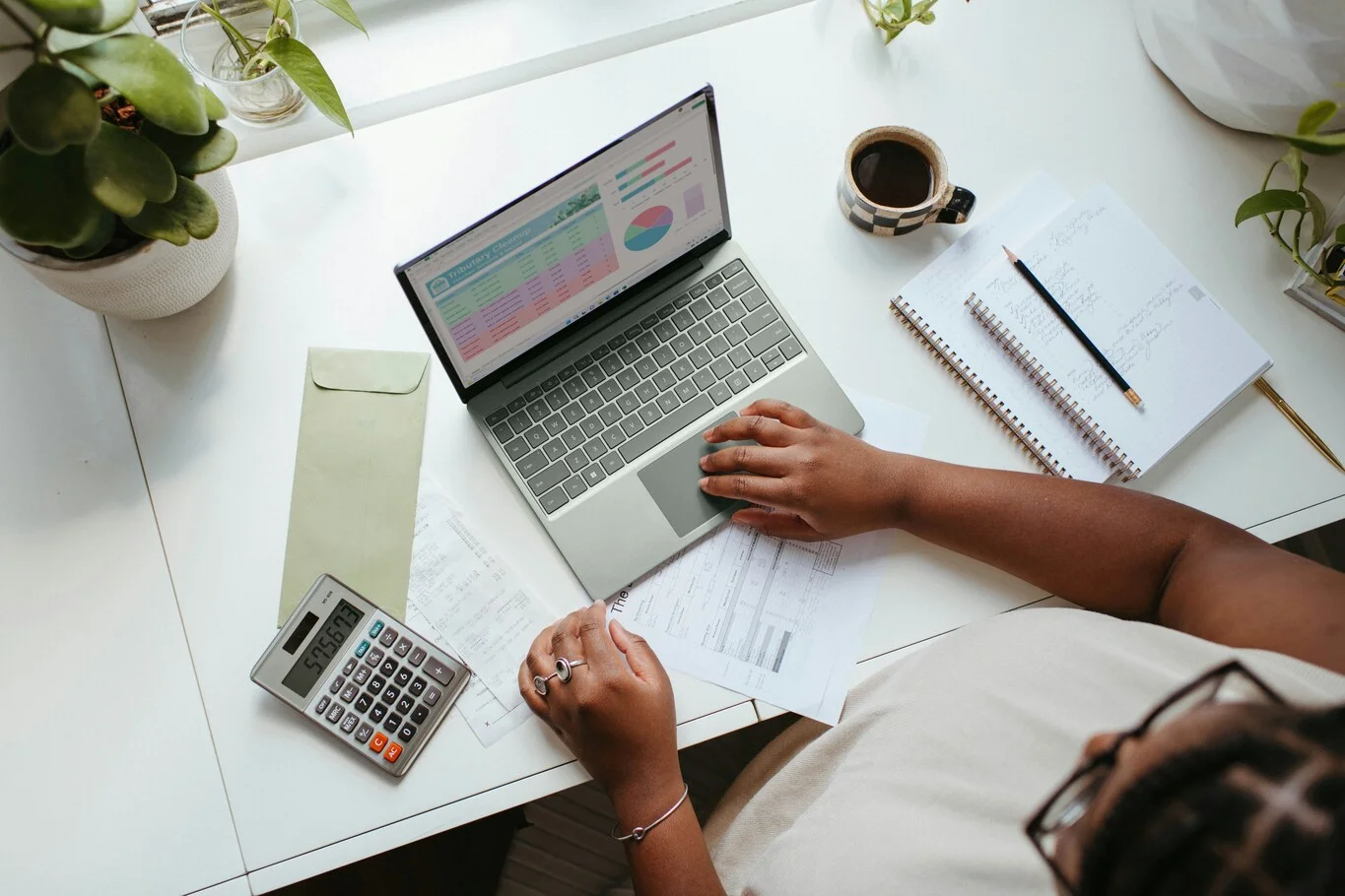 Person using a laptop, calculator, and notebook at a desk.