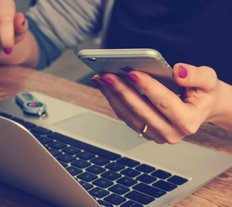 A person looking at their phone in front of a laptop