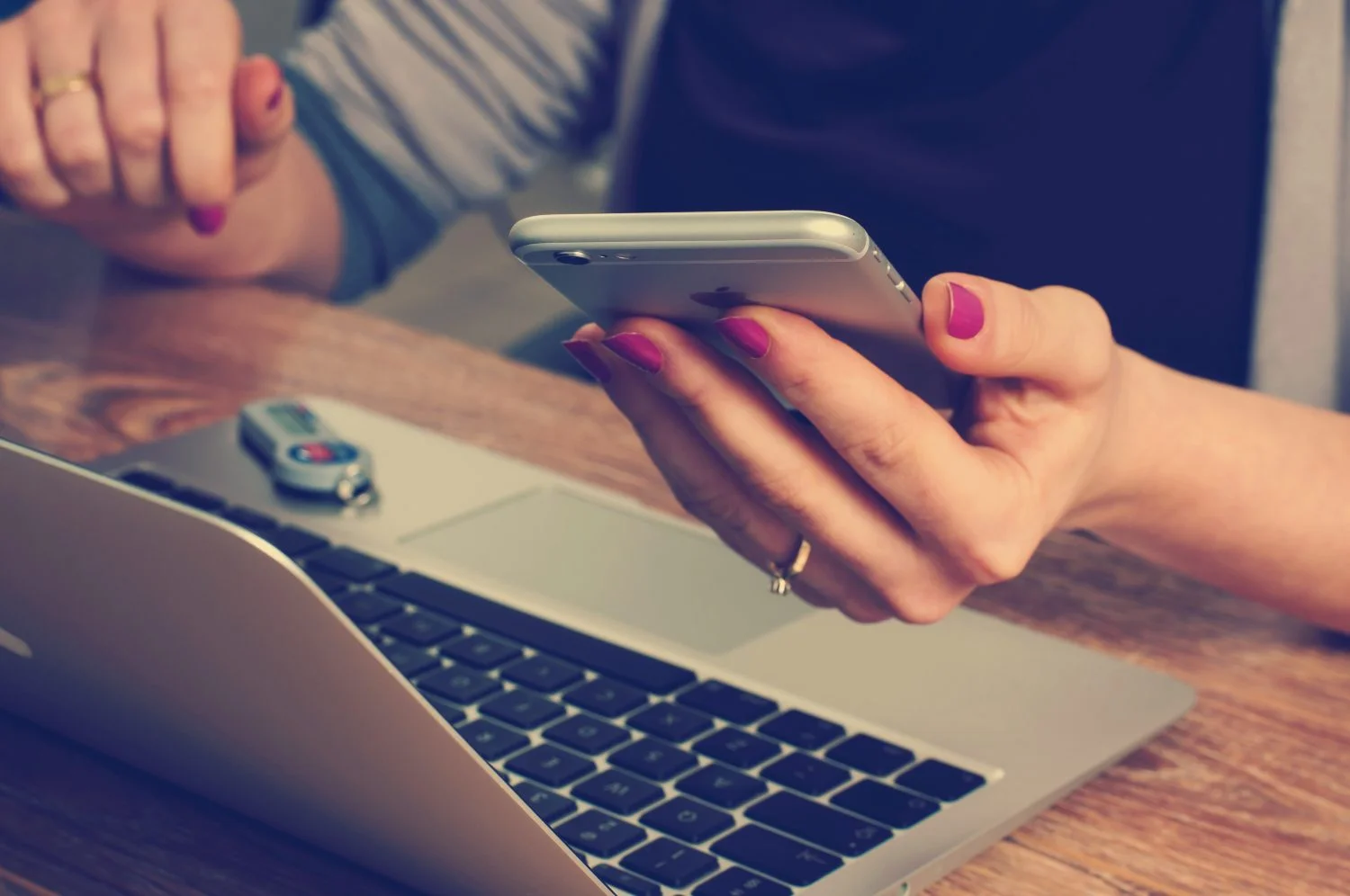 A person looking at their phone in front of a laptop
