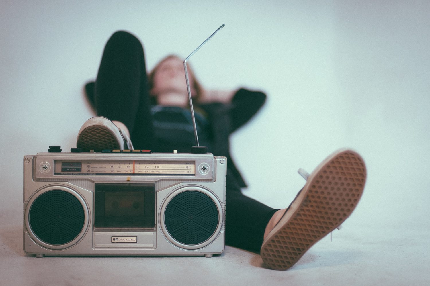 A person lying on their back, resting their foot on a vintage boombox
