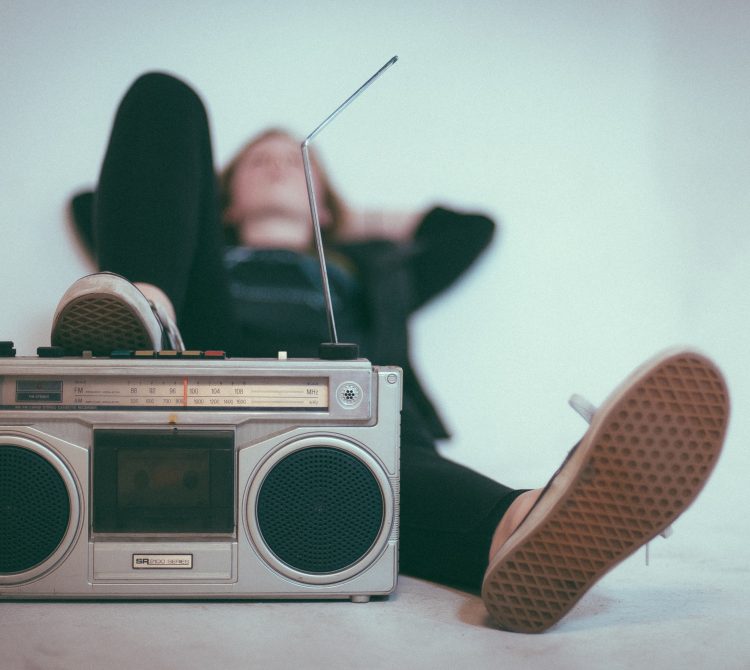 A person lying on their back, resting their foot on a vintage boombox