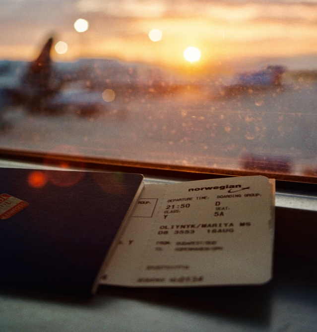 A plane ticket in front of a window overlooking an airport runway at sunset
