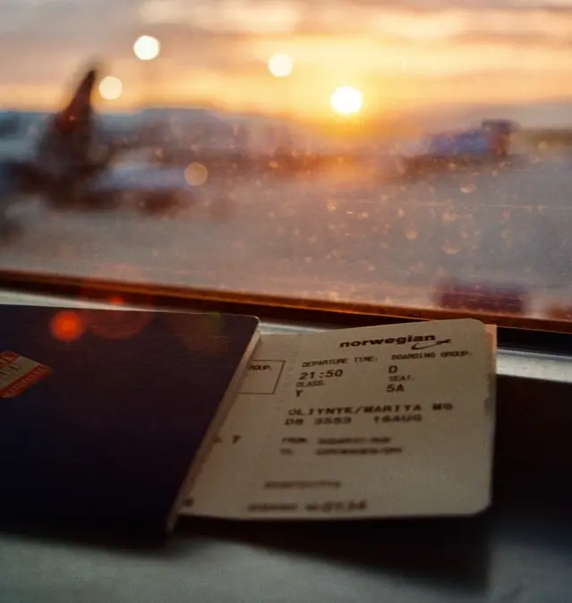 A passport and boarding pass on a windowsill overlooking an airport runway.