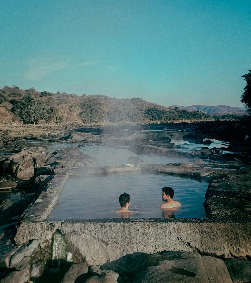 Two people sitting in a hot spring surrounded by rocks.