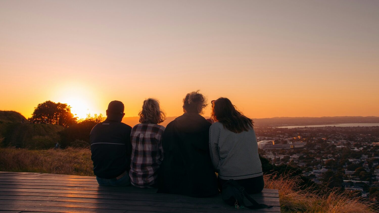 Four friends sitting side by side overlooking a city skyline at sunset
