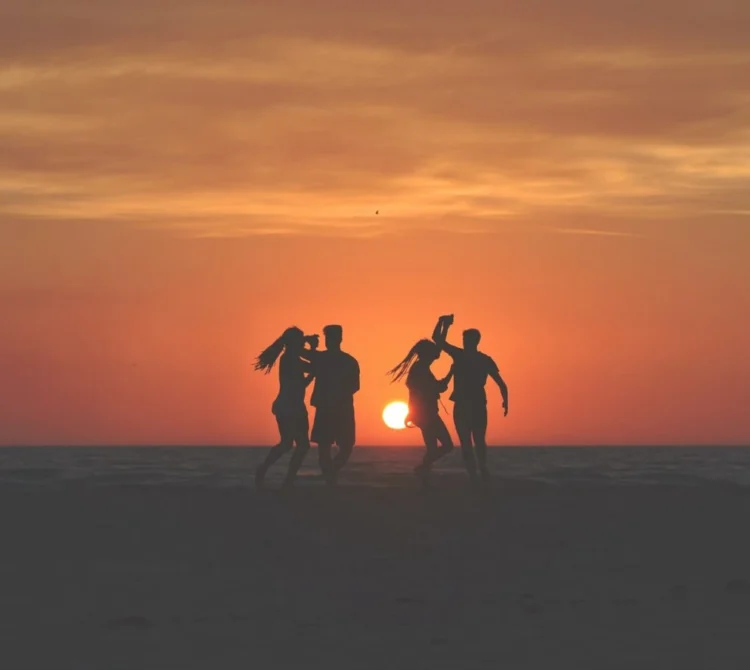 A group of people dancing together on the beach at sunset