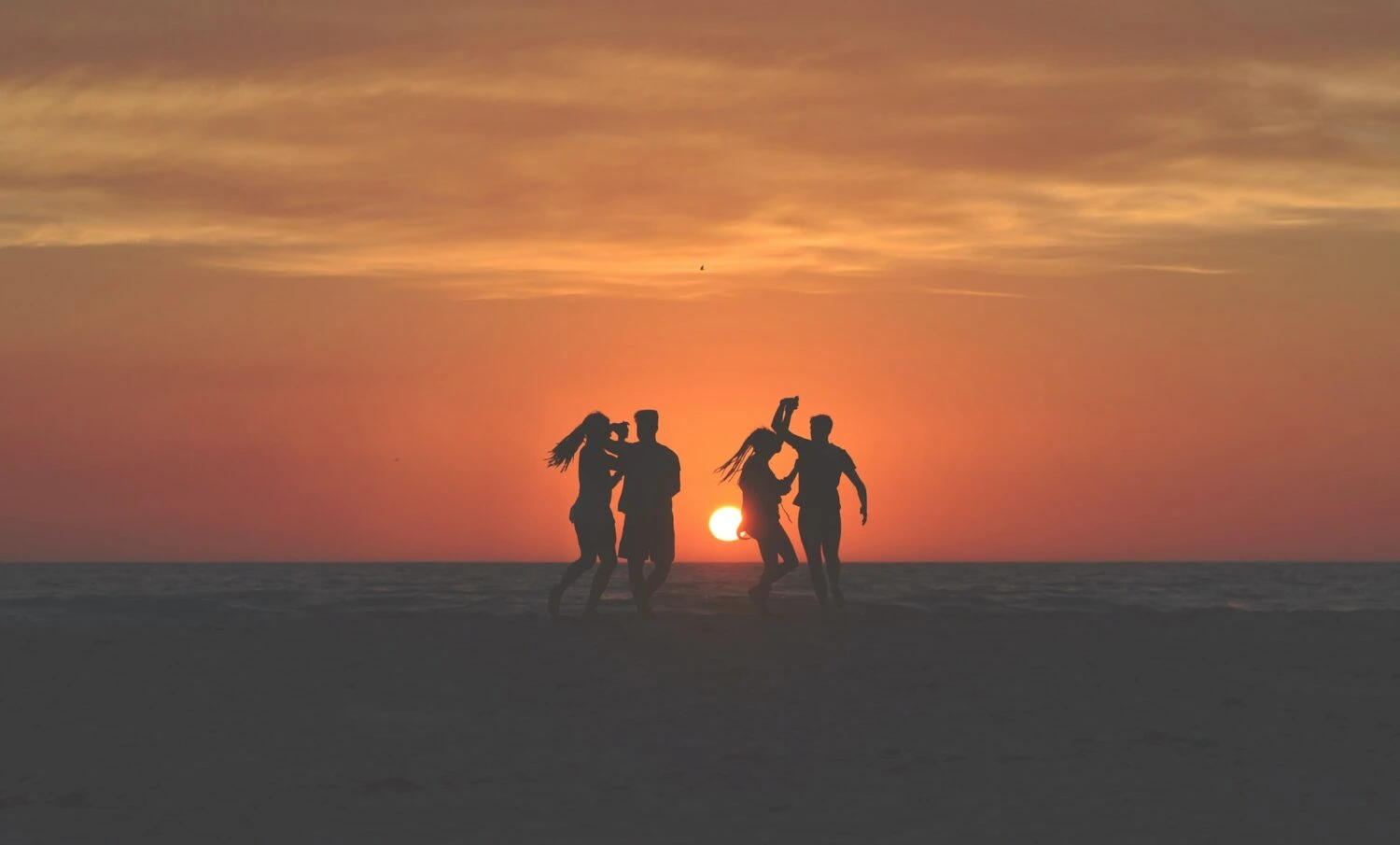A group of people dancing together on the beach at sunset
