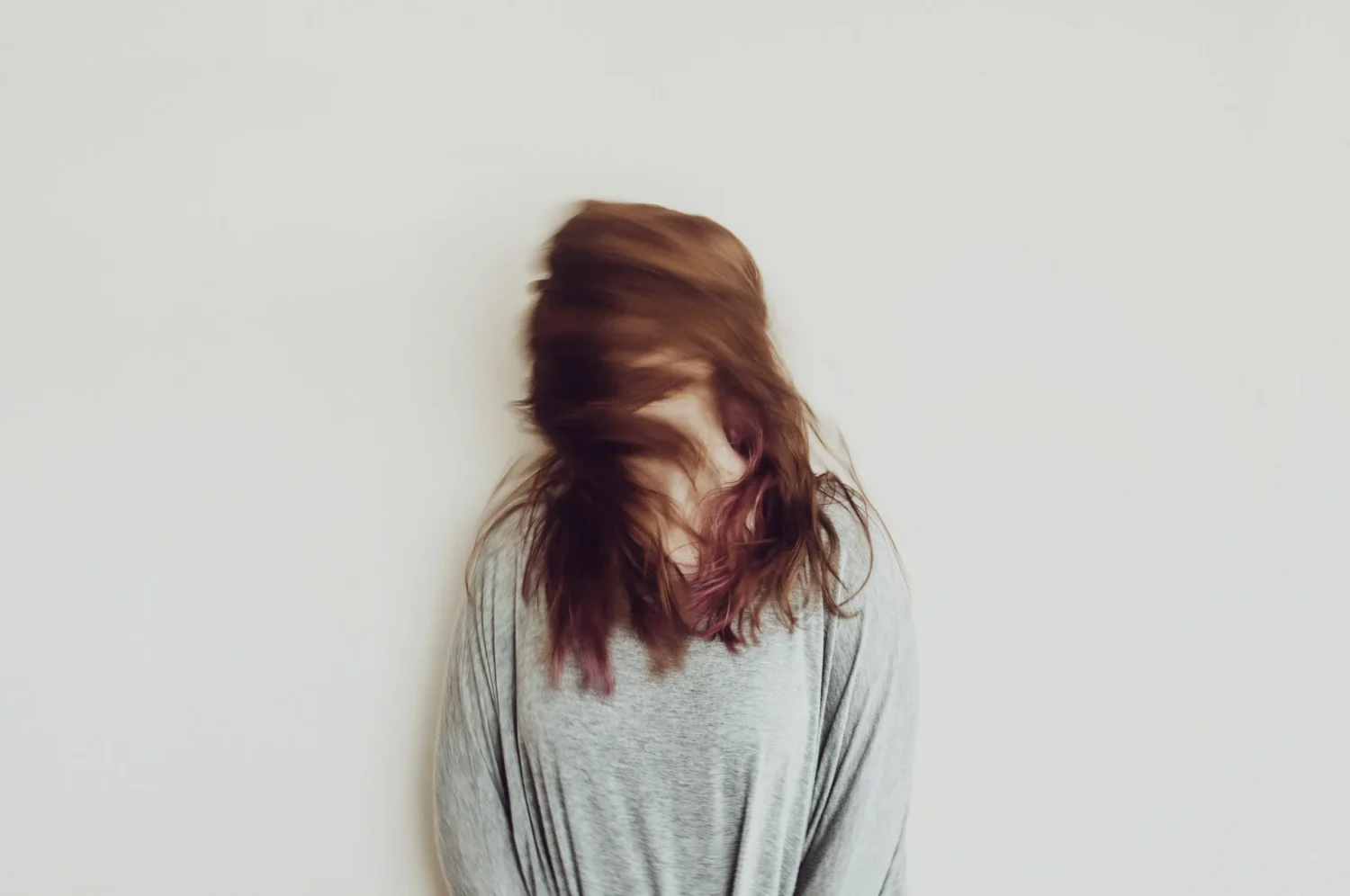 A women standing against a white wall with her hair covering her face