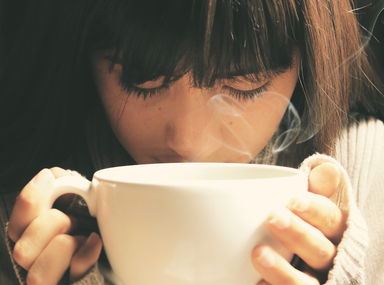 A woman leaning over a steaming cup of tea
