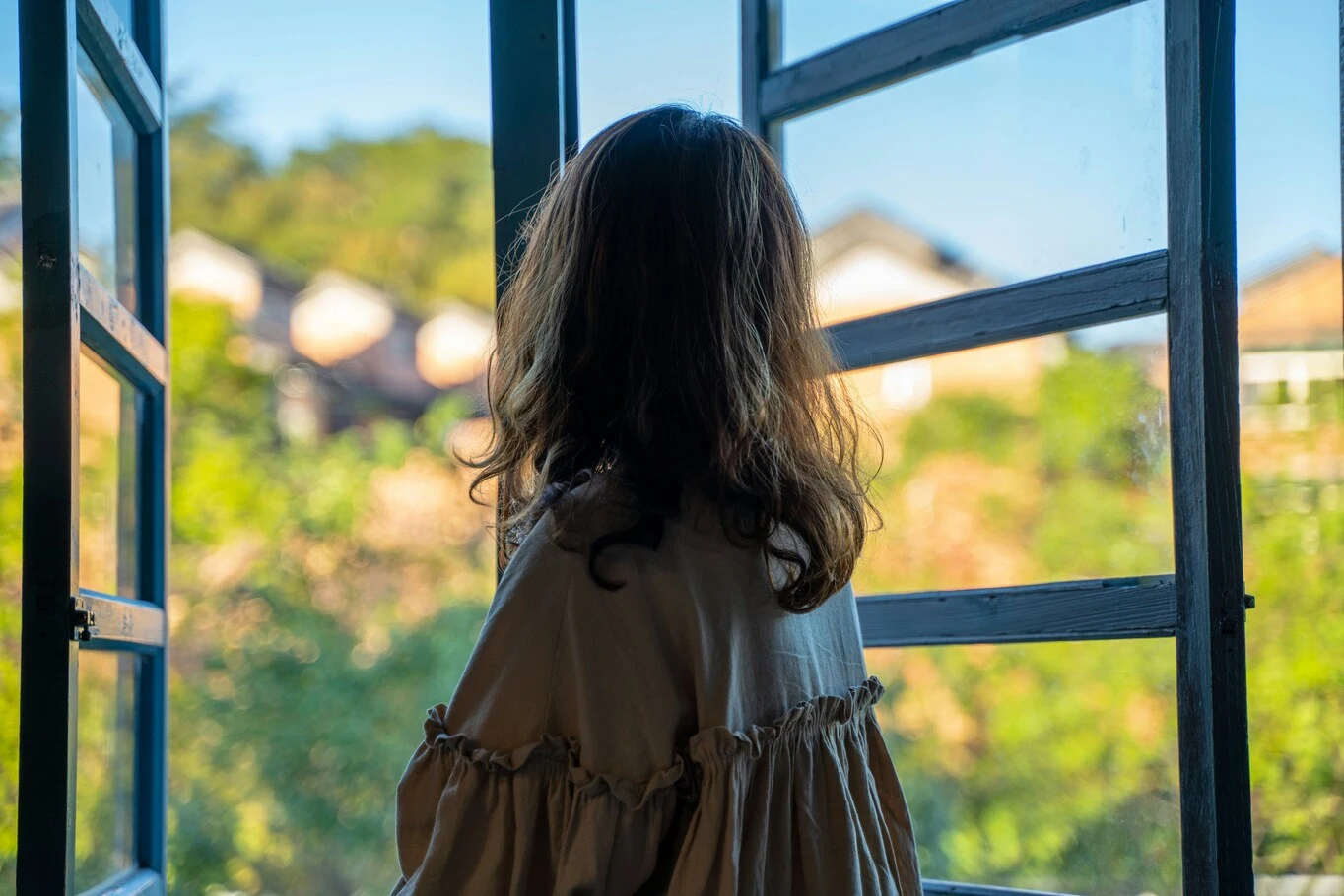 A woman standing at an open window looking outside