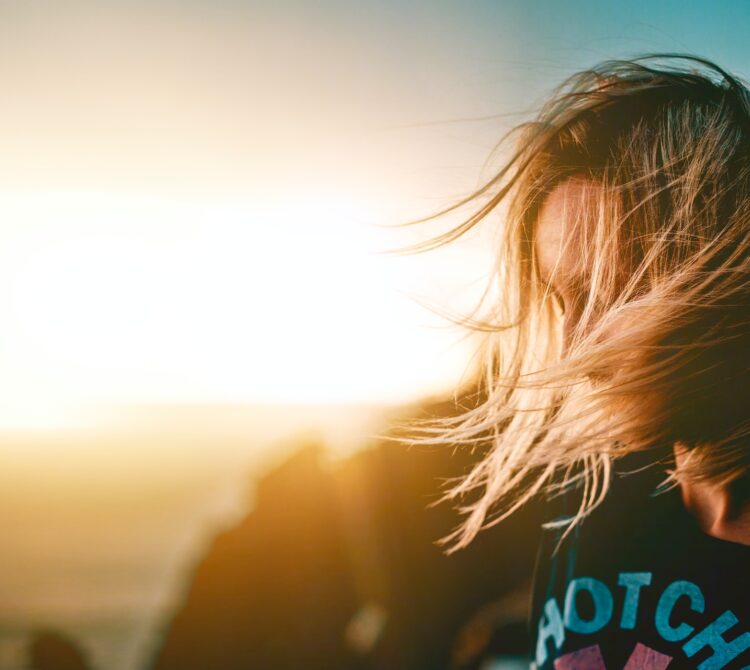 Person's hair blowing in front of their face with a sunset in the background