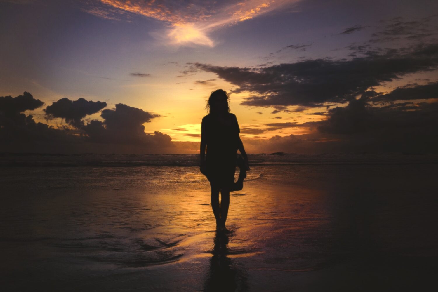 A silhouette of a person standing in the shorebreak at the beach looking out to a sunset