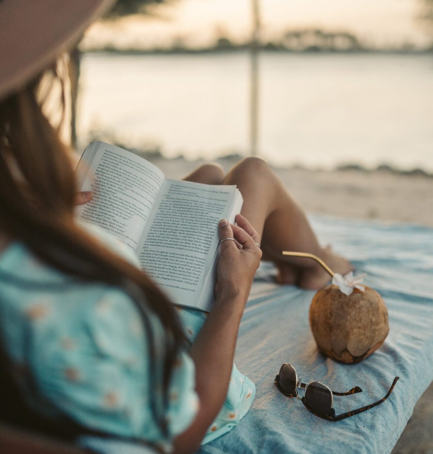 A woman sitting on a beach with a coconut reading a book