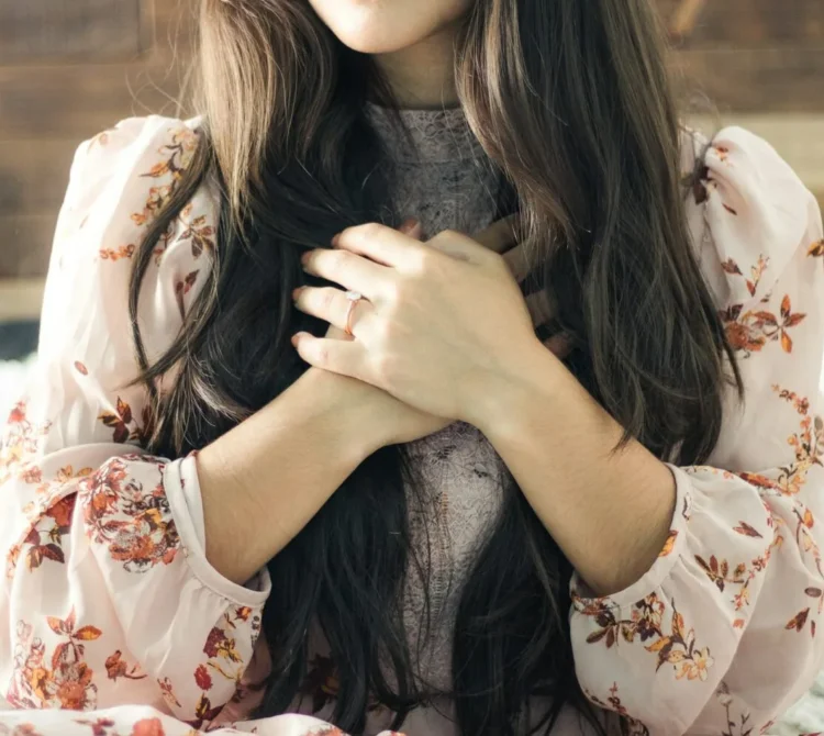 A woman with long brown hair, hands folded over her chest