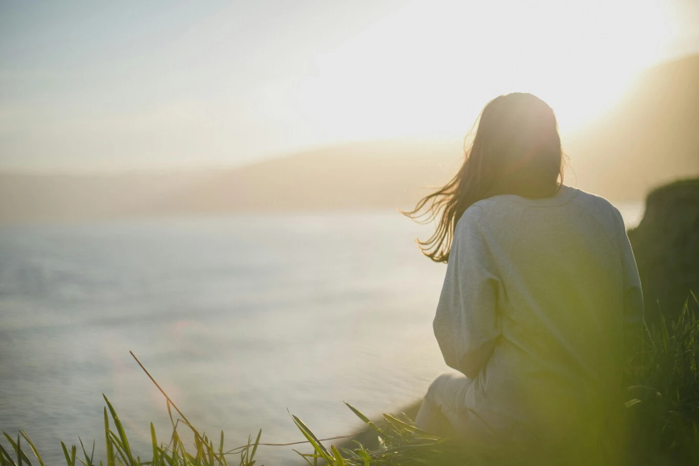 A woman sitting by the ocean looking toward the horizon.