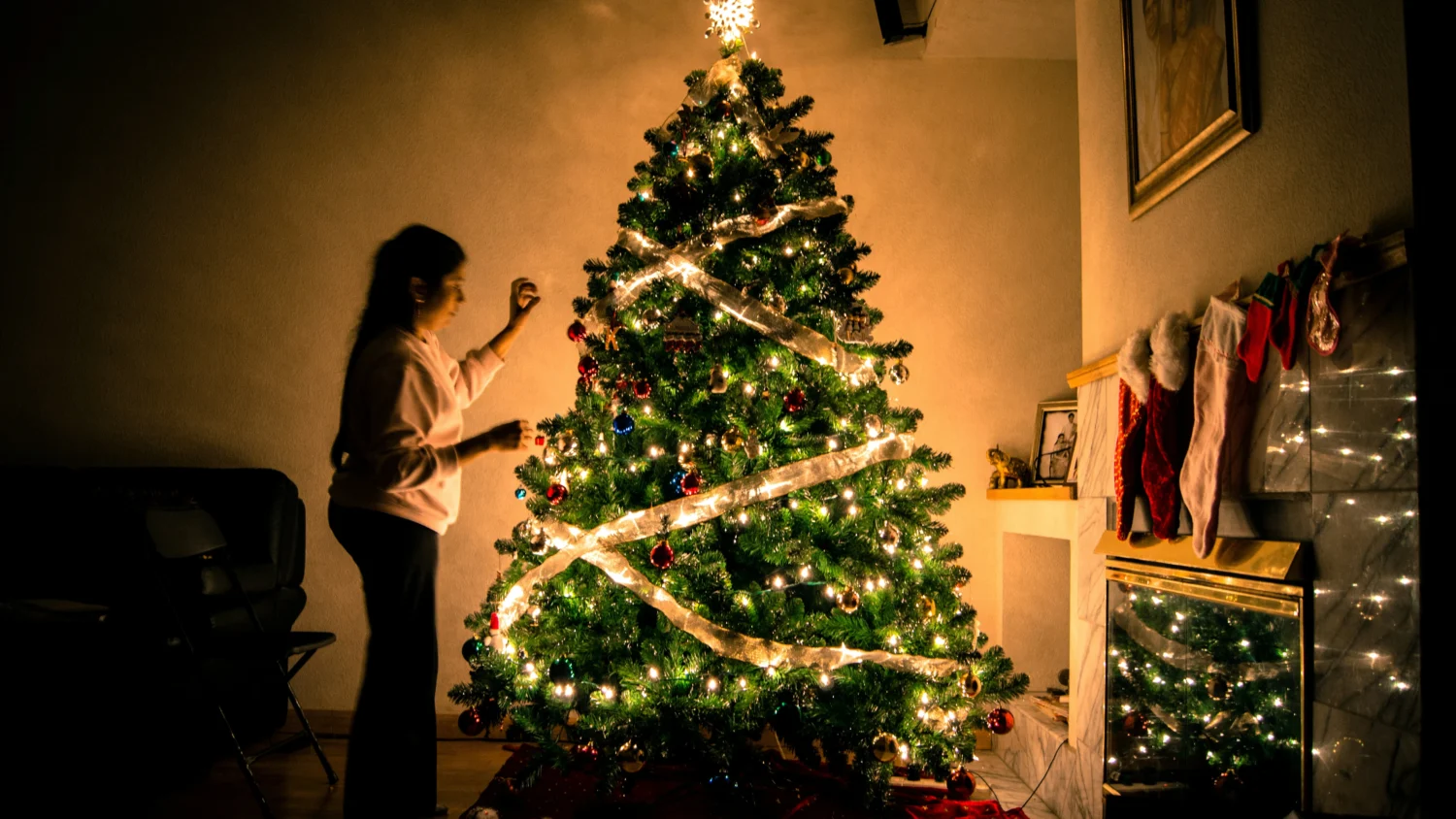 A women standing alone decorating a Christmas tree at night-time