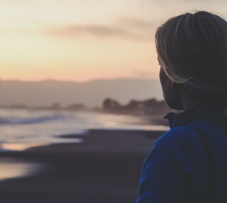 A woman stares out over a beach at dusk