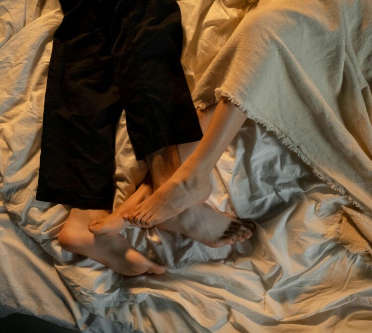 Male in long black pants and female in bed with feet intertwined