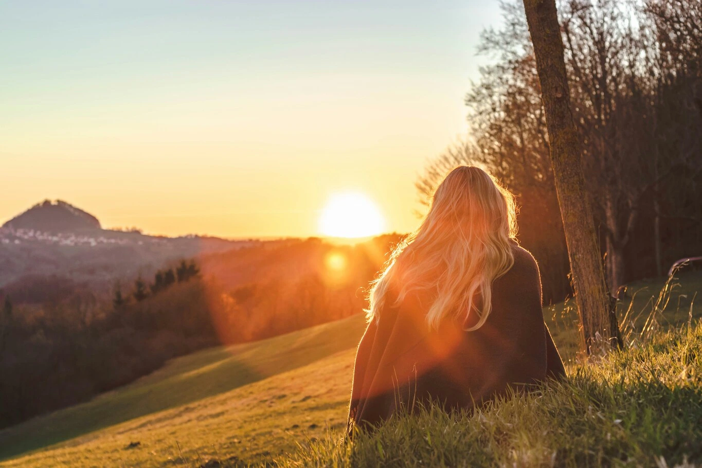 A woman sitting on a grassy hillside watching the sunset.