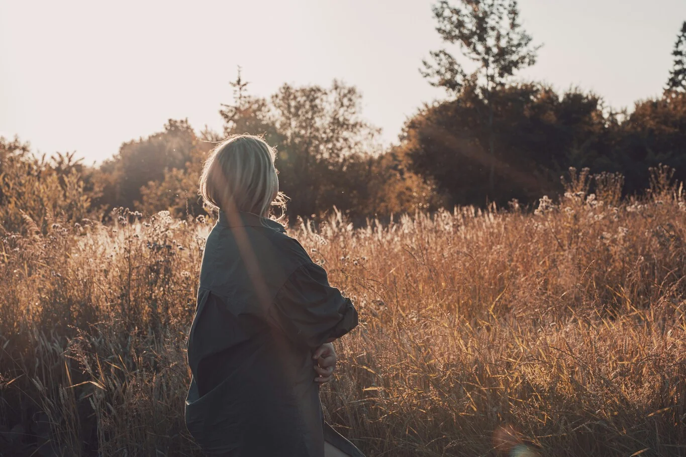 A person standing in a grassy field looking toward the trees.