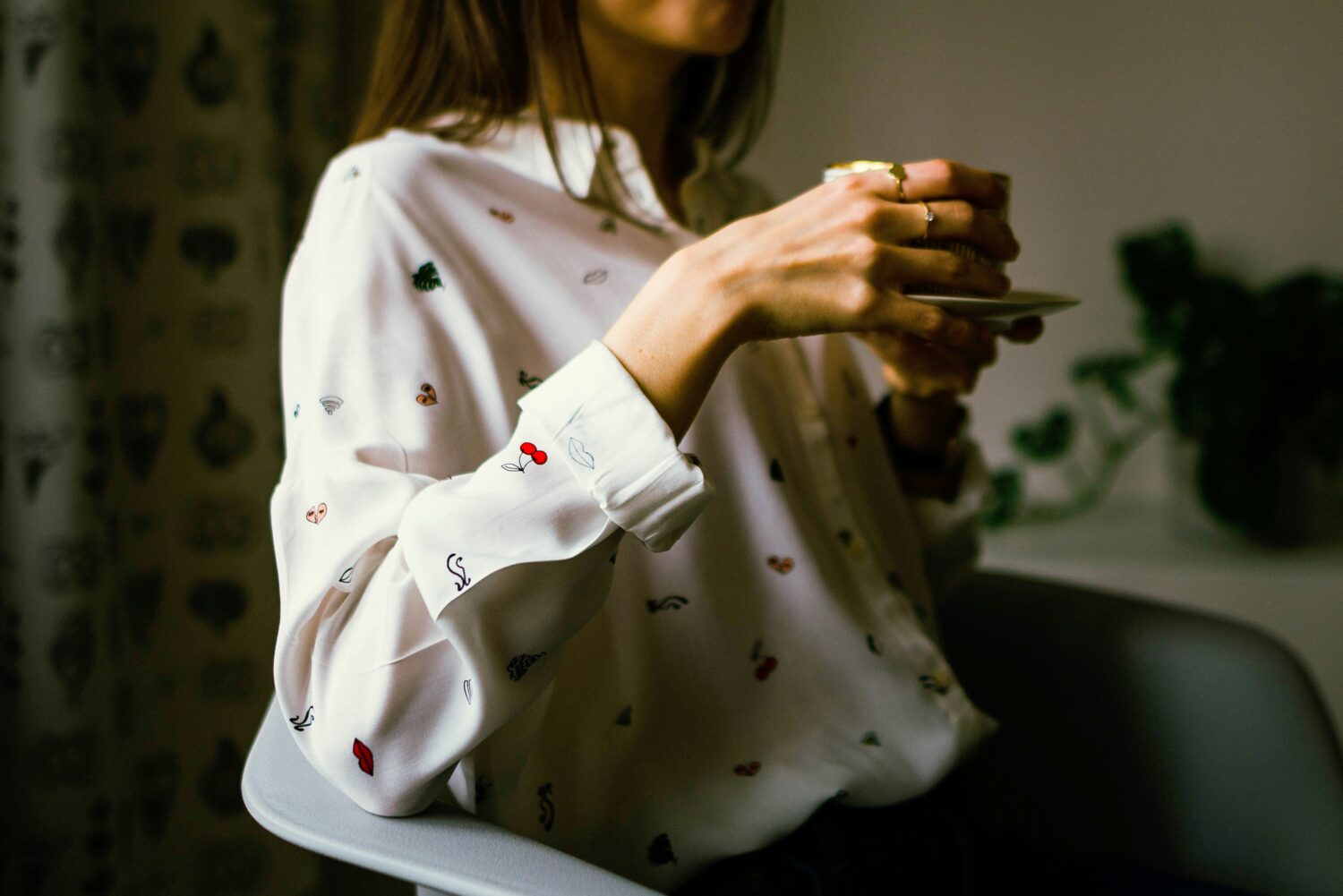 Person sitting in armchair, holding a cup of tea.