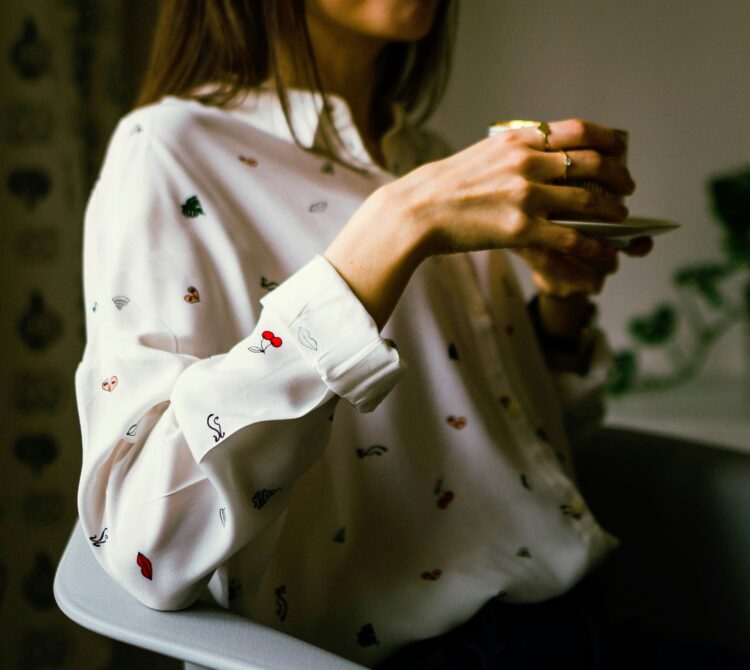 Person sitting in armchair, holding a cup of tea.