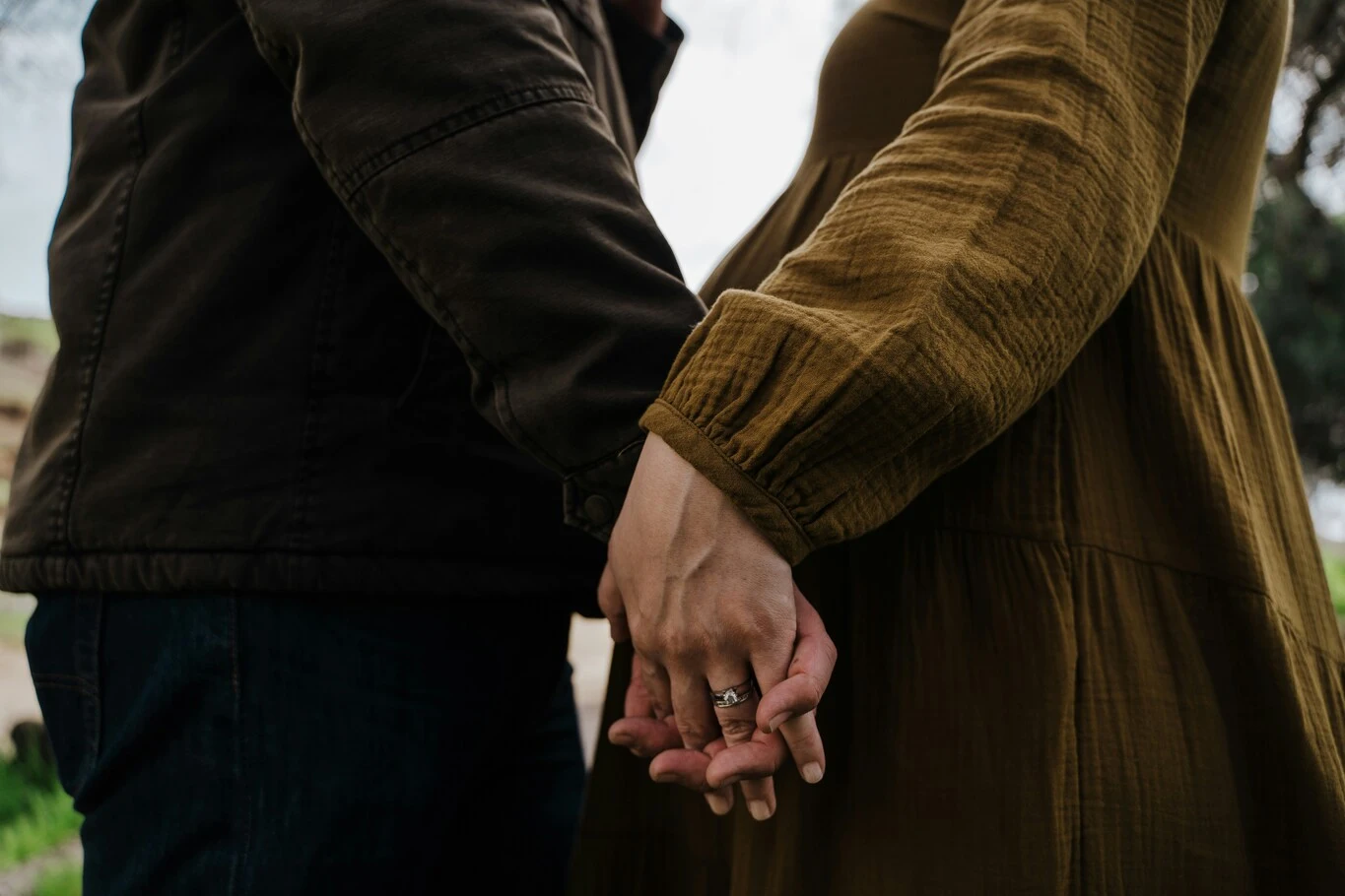Close-up of two people holding hands with their fingers intertwined outdoors.