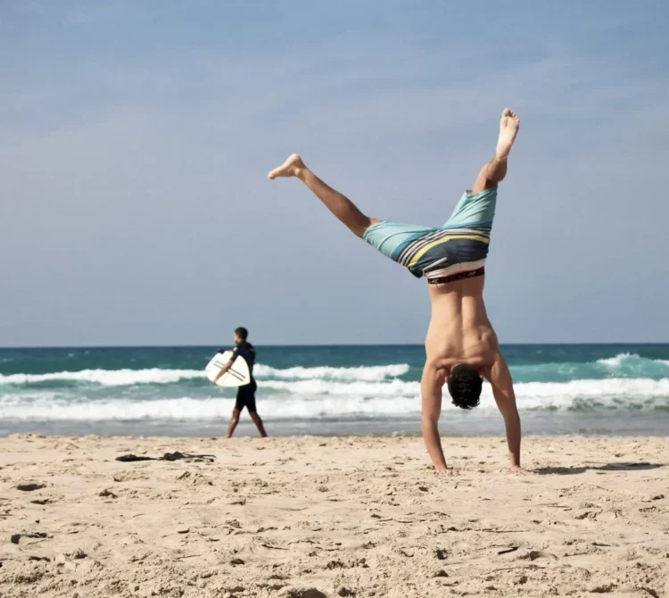 A person doing a handstand on a sandy beach with ocean waves in the background.