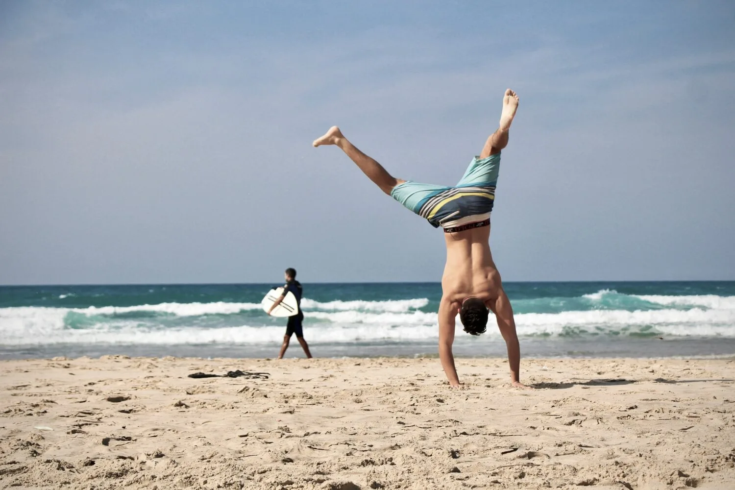 A person doing a handstand on a sandy beach with ocean waves in the background.