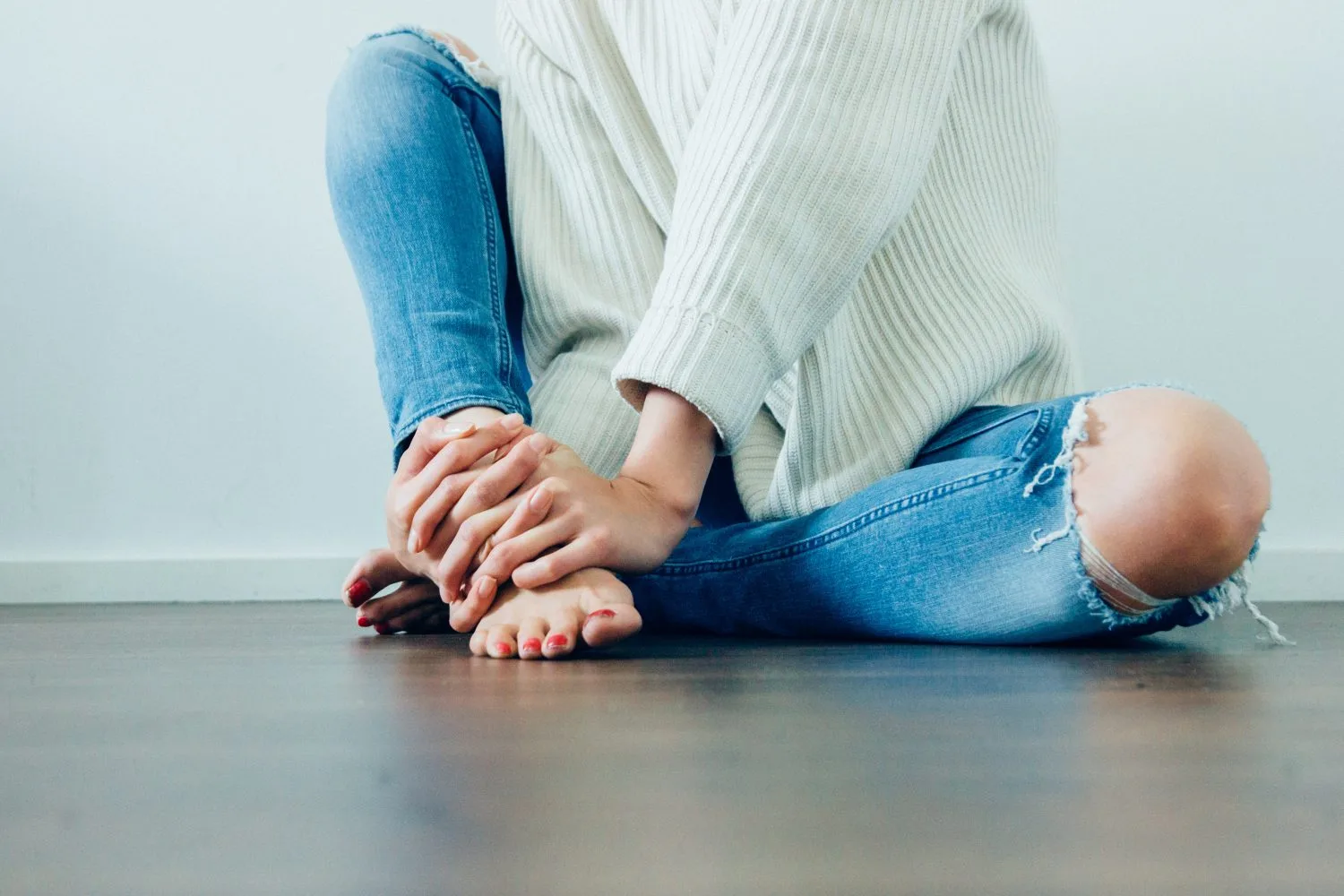 A person sitting cross-legged on the floor wearing a sweater and blue jeans.