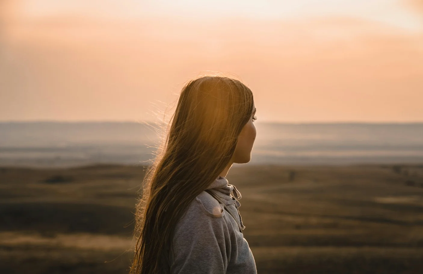 A woman looking toward the horizon at sunset.