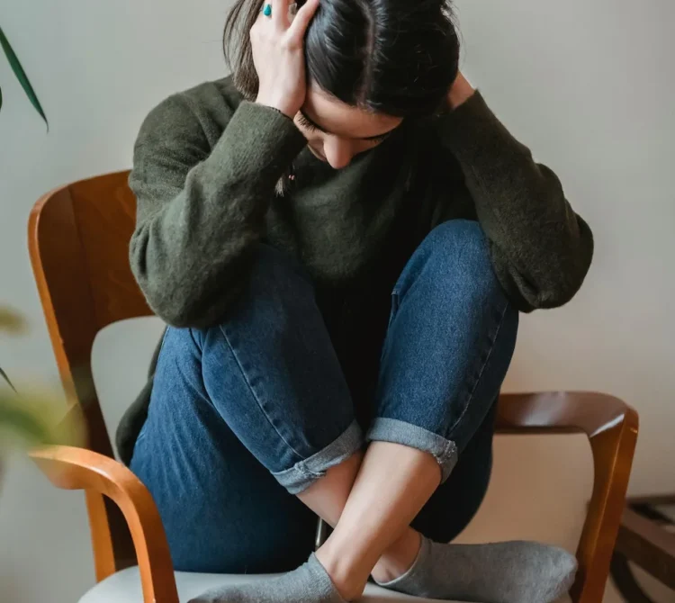 Women crossed legged on chair with head in hands looking down