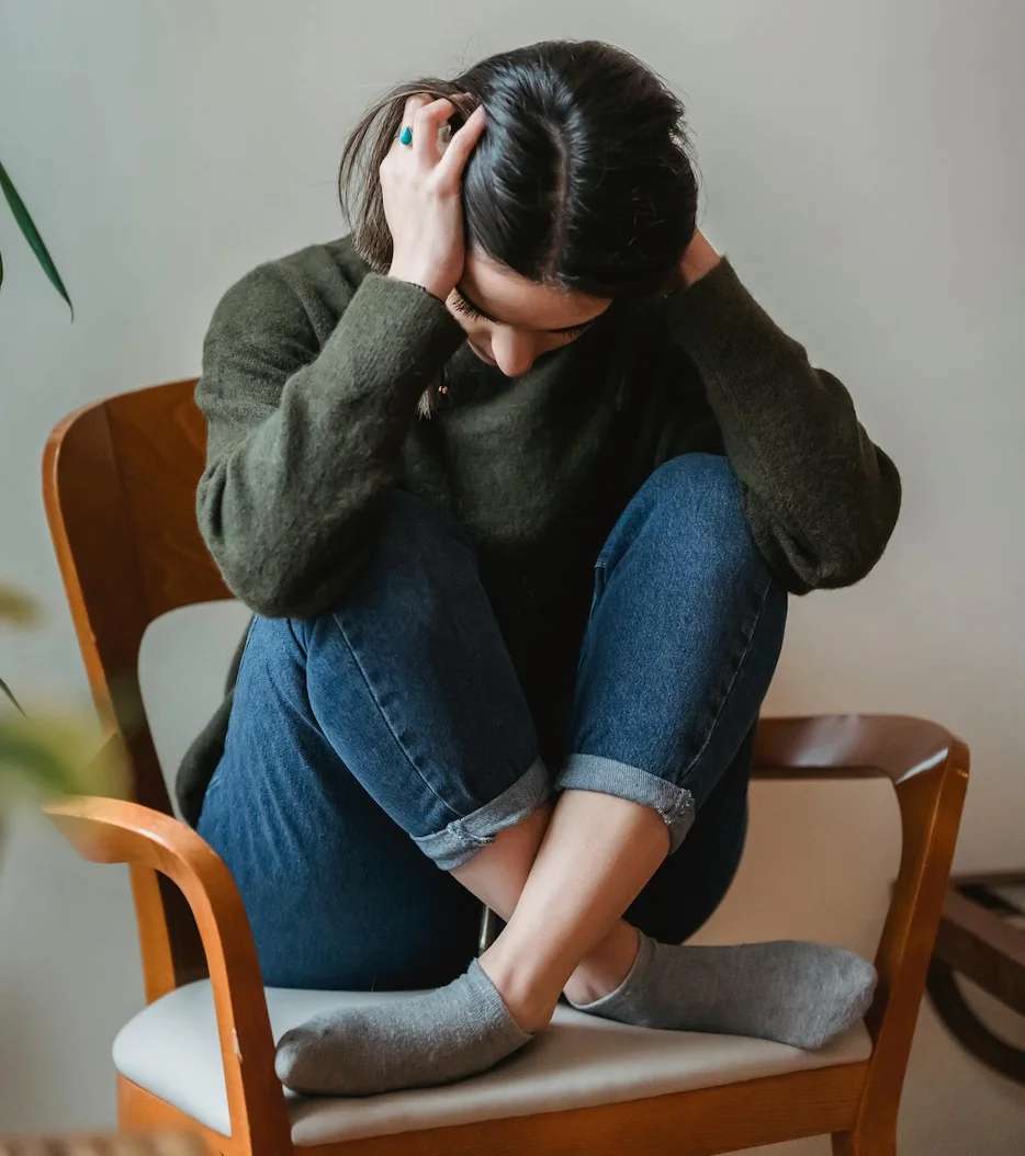 Women crossed legged on chair with head in hands looking down