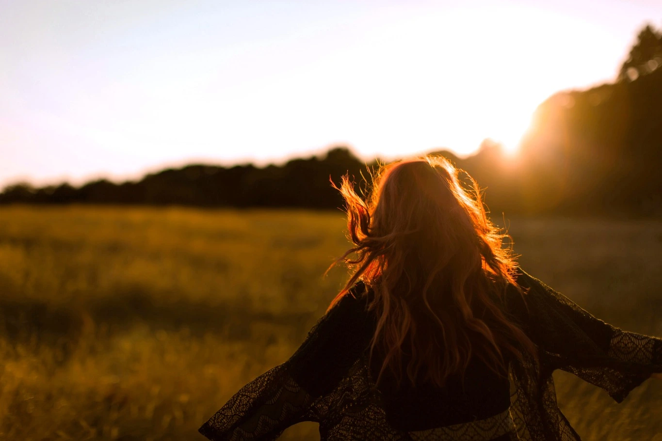 A woman walking through a field toward the sunset.