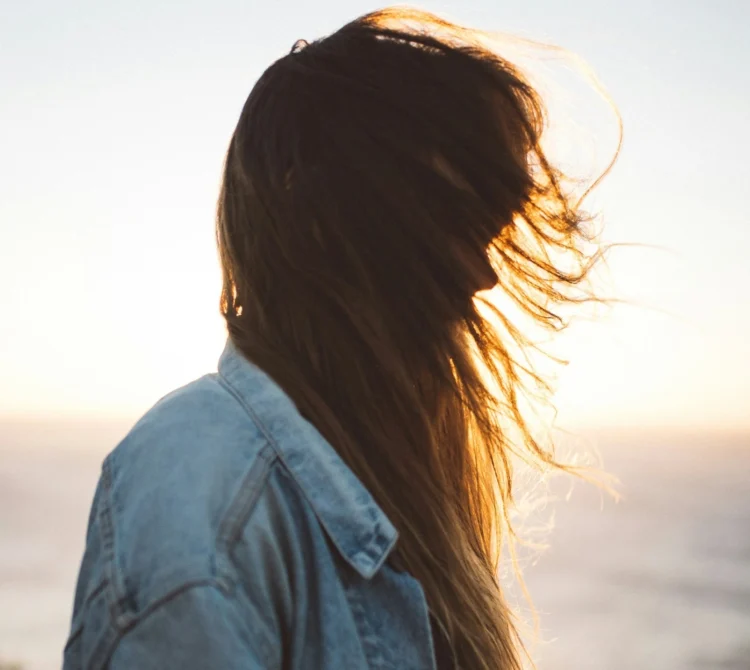 A woman standing side on with her hair blowing across her face