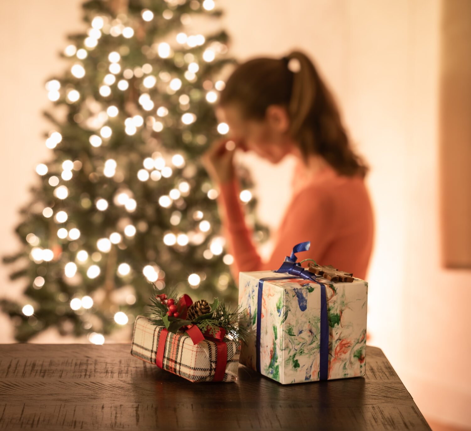 A woman with her head in her hands, standing in front of a Christmas tree with presents